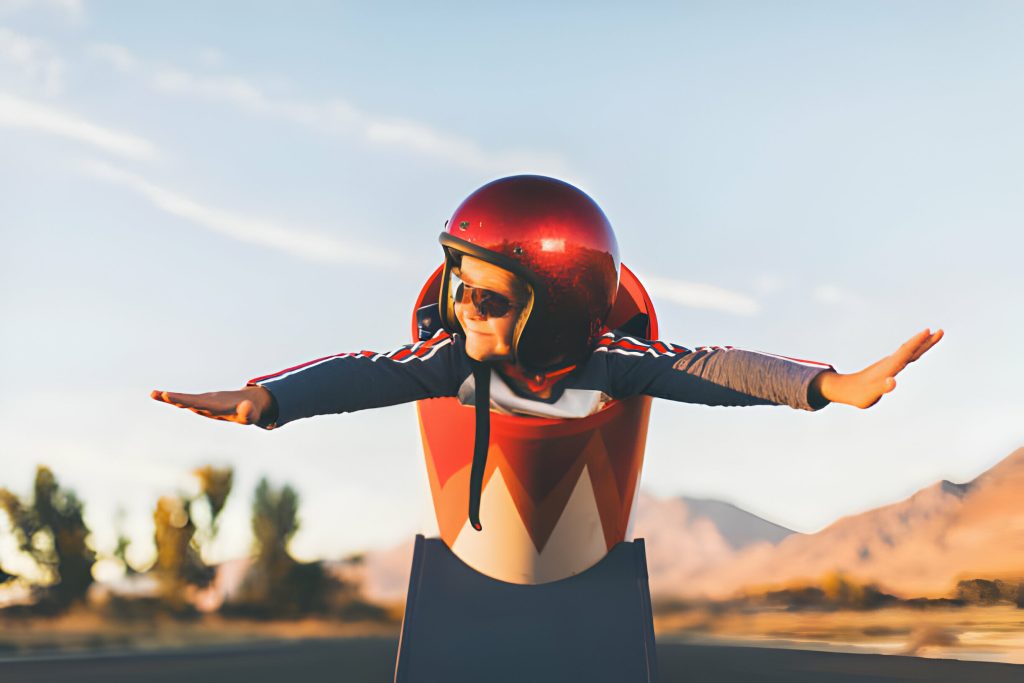 A young boy dressed in helmet and flight goggles sits ready for flight in a homemade cannon. His arms are outstretched and ready for take off as he is excited to explore new heights. Image taken on a rural road in Utah, USA.
